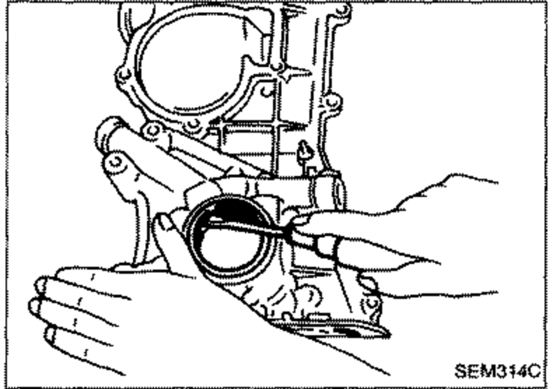Illustration of removing the front oil seal from the front cover. A hand uses a tool to pry/extract the seal from the circular bore of the front cover.