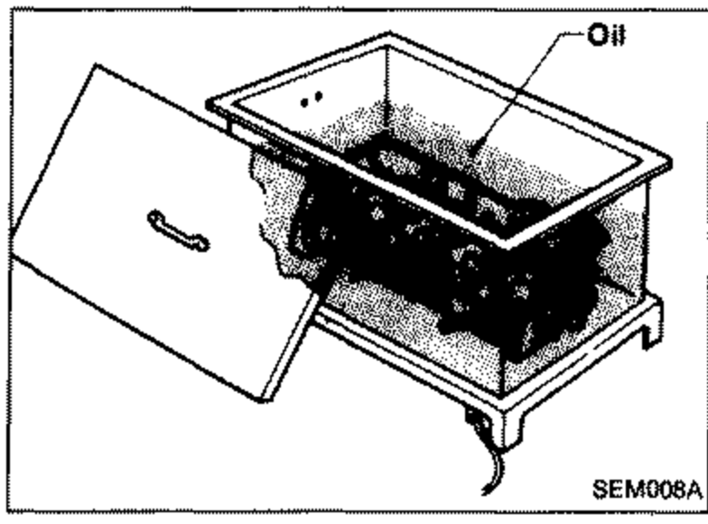 Illustration of heating the cylinder head in an oil bath to remove the valve guide. The cylinder head is submerged in a heated oil tank; label 'Oil' points to the tank.
