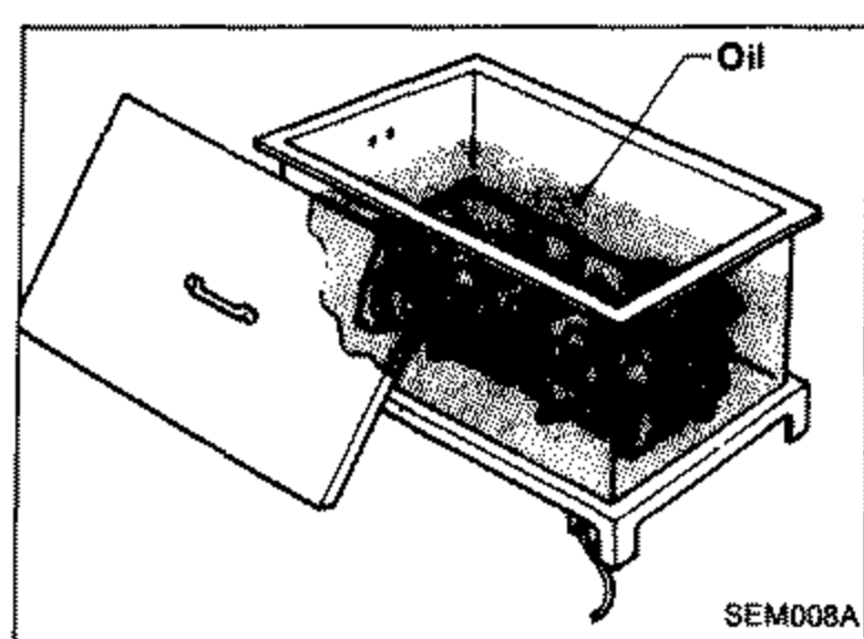 Illustration of heating the cylinder head in a heated oil bath/tank for press-fitting the valve seat. Label 'Oil' points to the tank.