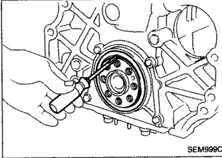 Rear of engine / rear oil seal retainer area with the flywheel ring gear visible, illustrating removal of the rear oil seal from the retainer.