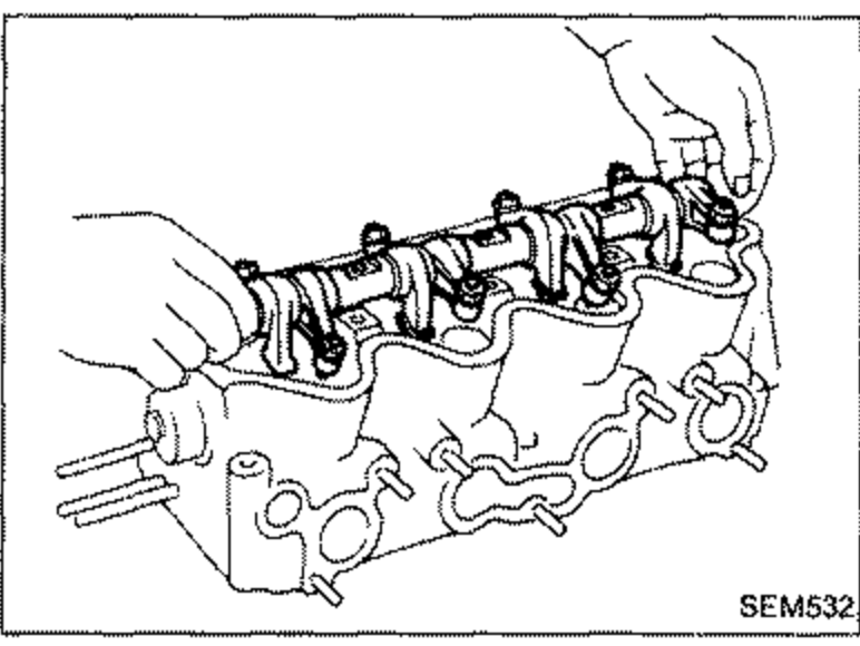 Hands removing the rocker shaft with rocker arms from the cylinder head.