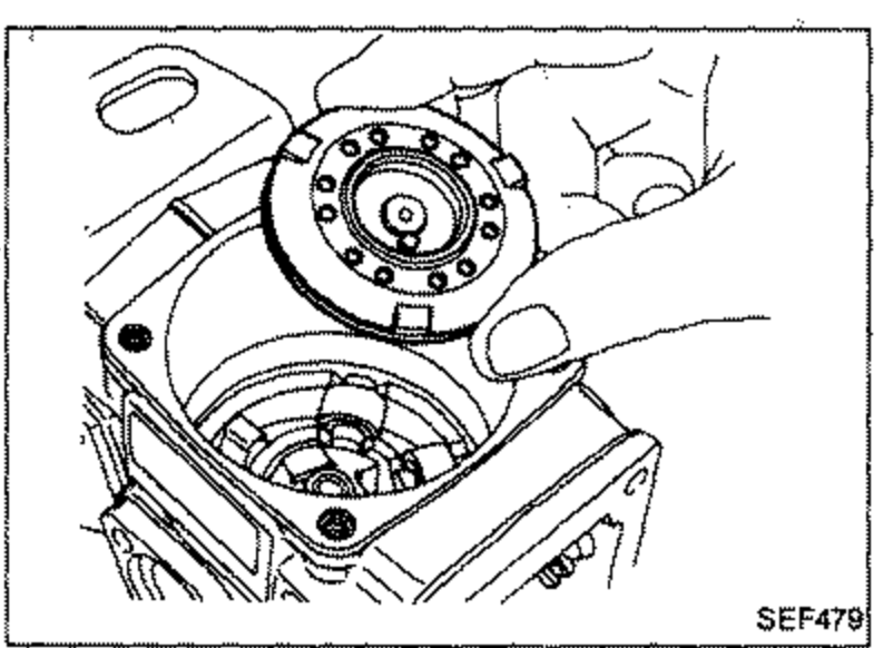 Removal of the shim, cam disc, spring and driving disc. A hand holds the round cam disc / driving disc assembly with raised pins visible on its face.