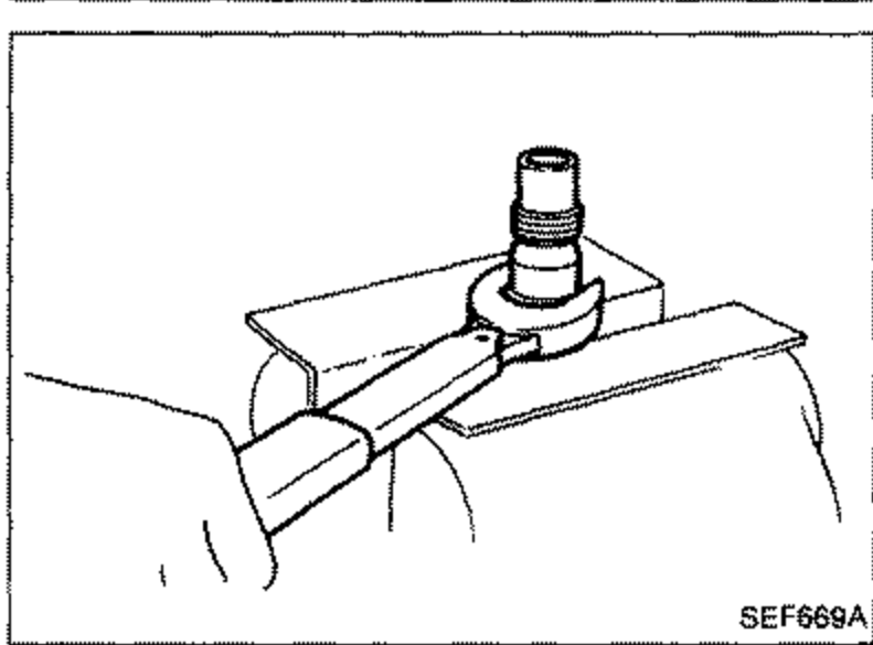 Illustration of the injection nozzle held in a fixture/vise, showing the nozzle nut being loosened while preventing the nozzle top from turning.